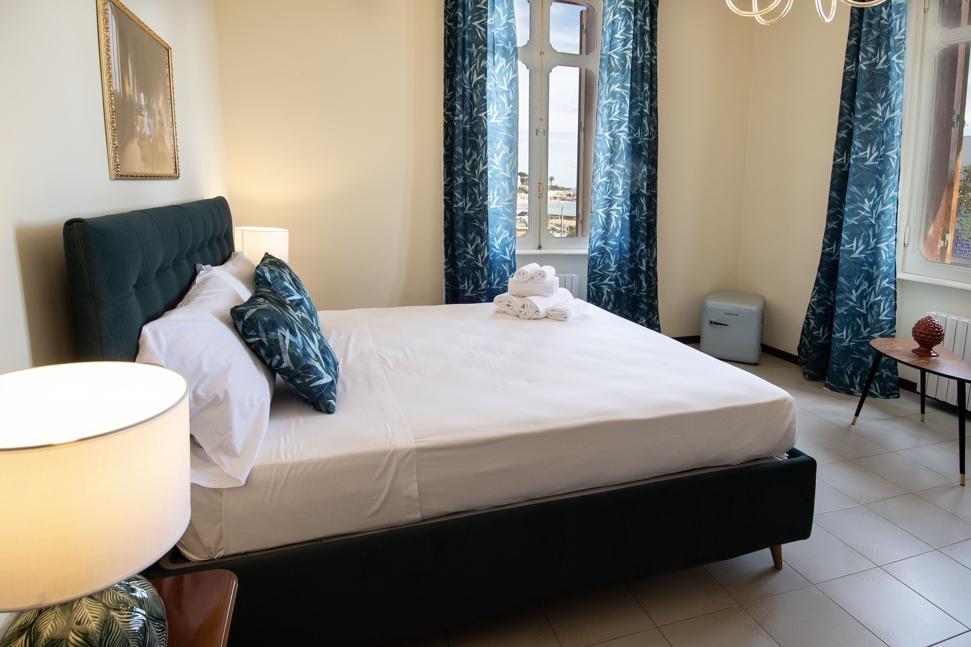A neatly made bed with white linens, a bedside lamp, and a stack of folded towels.