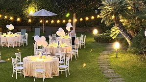 An outdoor event with round tables, white chairs, and string lights.