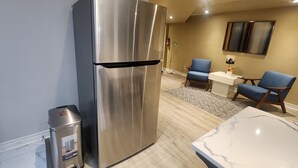 A modern kitchen with a stainless steel refrigerator, a marble countertop, and two blue chairs.