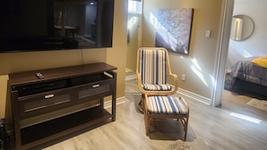 A modern living room with a flat-screen TV, a dark wooden entertainment unit, a striped armchair, and a large painting on the wall.