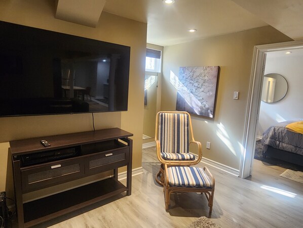 A modern living room with a flat-screen TV, a dark wooden entertainment unit, a striped armchair, and a large painting on the wall.