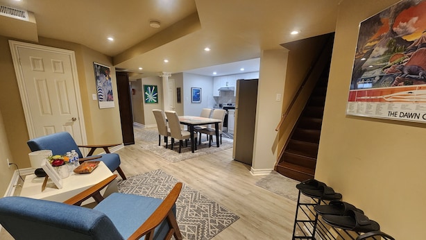 A spacious living area with a dining table, blue chairs, a kitchen in the background, and a staircase leading to another level.
