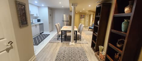 A modern kitchen with white cabinets, a stainless steel refrigerator, and a dining area with a table and chairs.