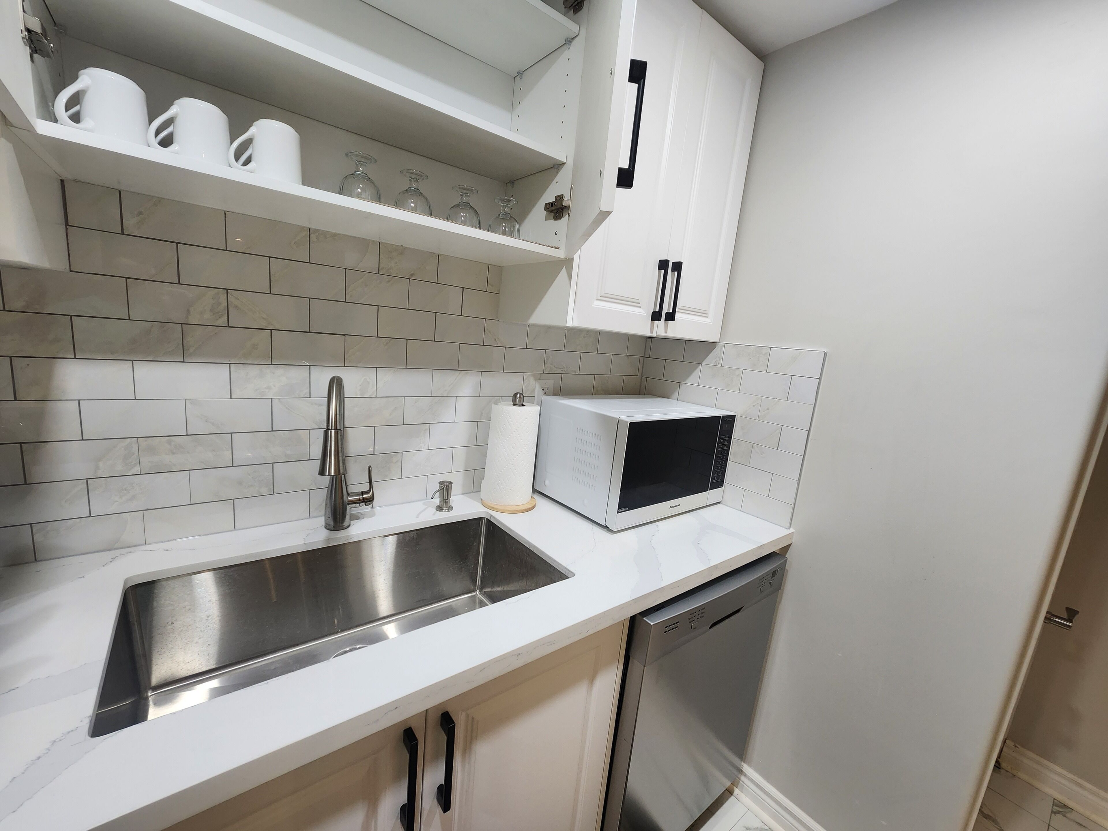 Una cocina moderna con un lavamanos de acero inoxidable, armarios blancos y un lavavajillas integrado.