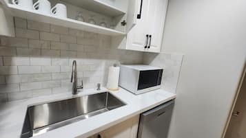 Una cocina moderna con un lavamanos de acero inoxidable, armarios blancos y un lavavajillas integrado.