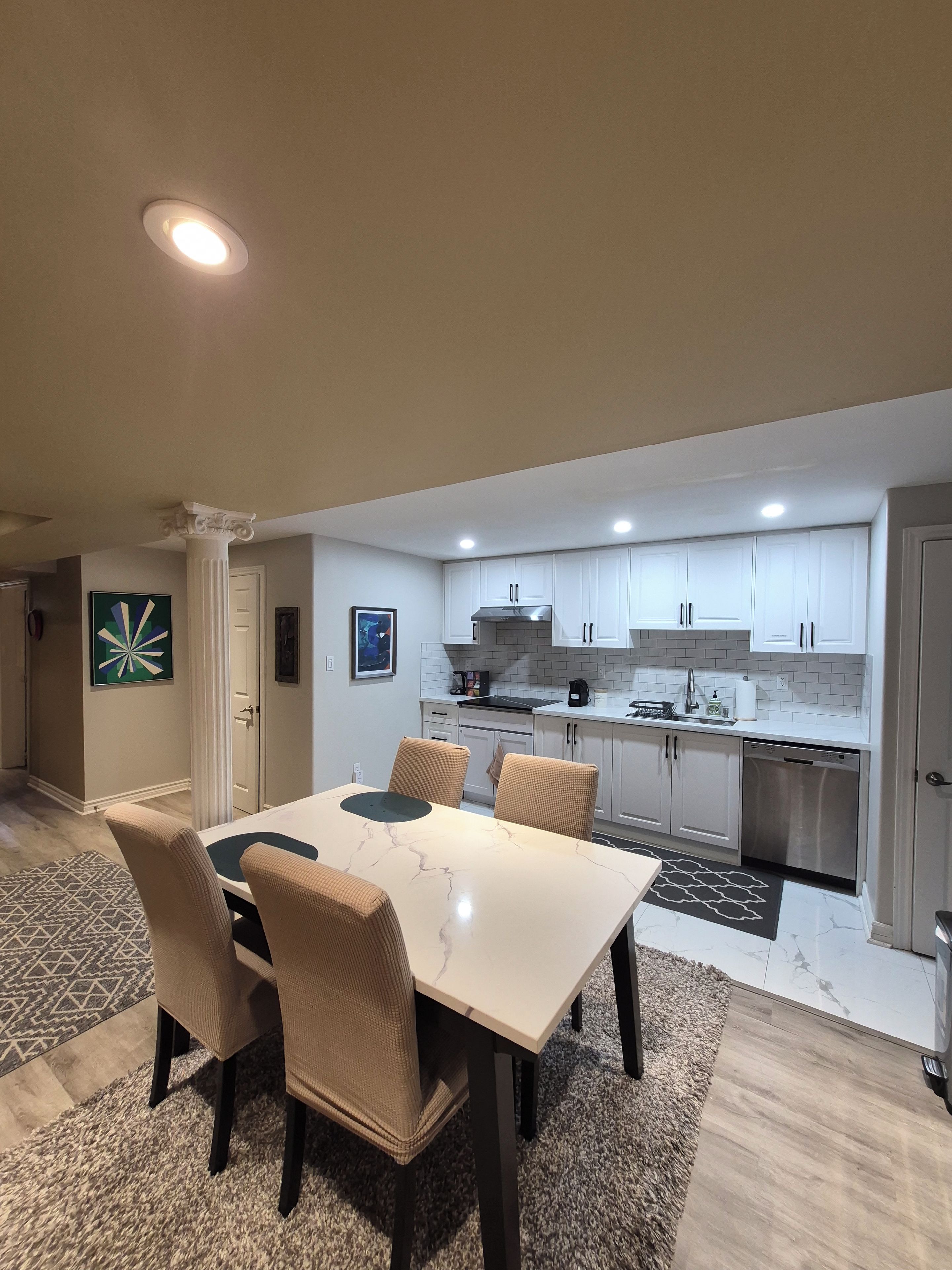A modern kitchen with white cabinets, a dining area with a marble table, and a patterned rug.