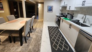 A modern kitchen with white cabinets, a stainless steel dishwasher, and a dining area with a marble table and chairs.