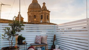 Ein Balkon mit Blick auf ein historisches Gebäude, einem Blumentopf, einer Bank mit Kissen und einem kleinen Tisch mit Gegenständen.