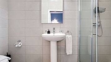 Un baño con un lavamanos blanco, un espejo, una cabina de ducha de vidrio y baldosas de suelo estampadas.