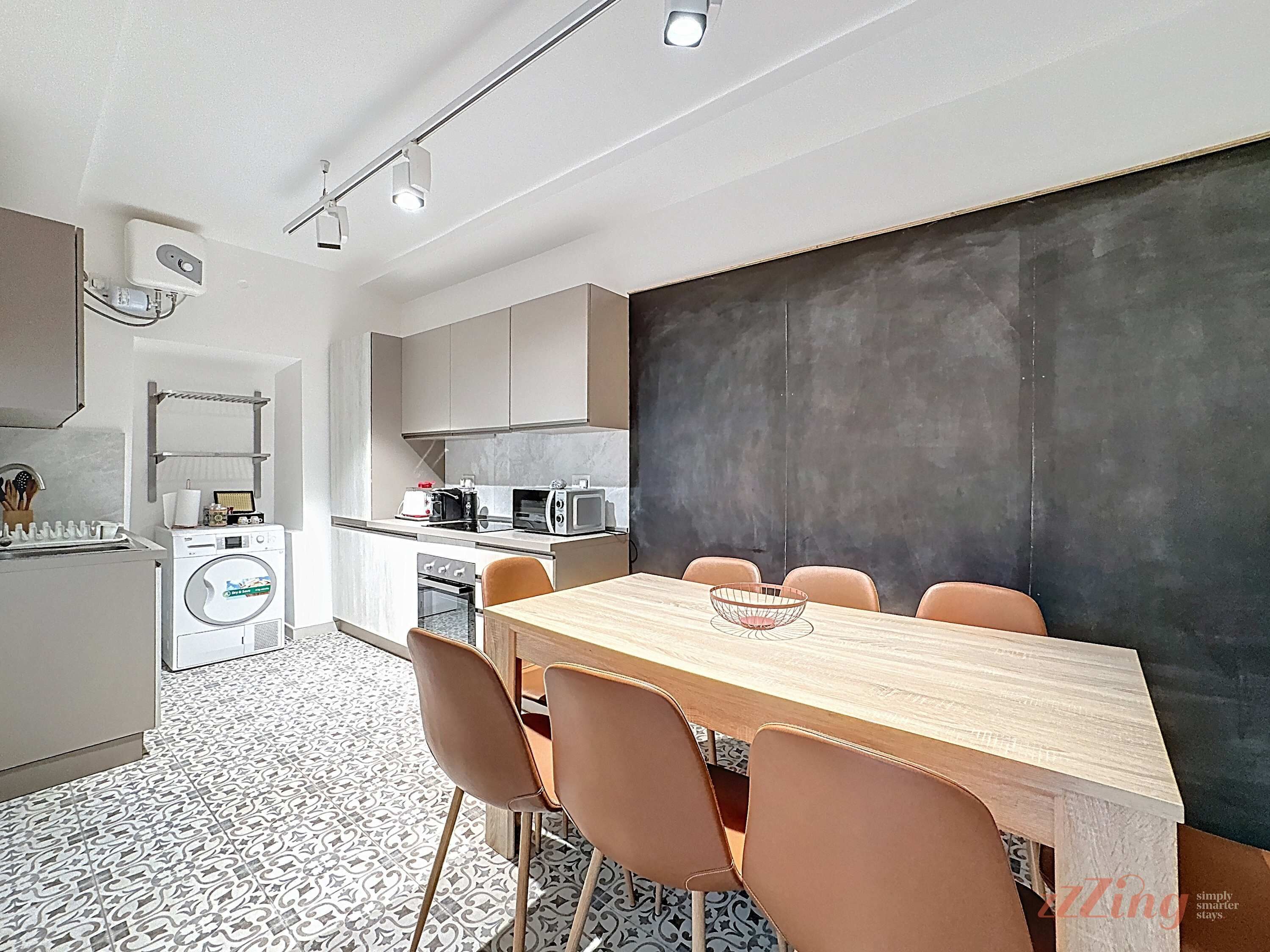 A modern kitchen with a dining area, featuring a wooden table and chairs, a washing machine, and a microwave.