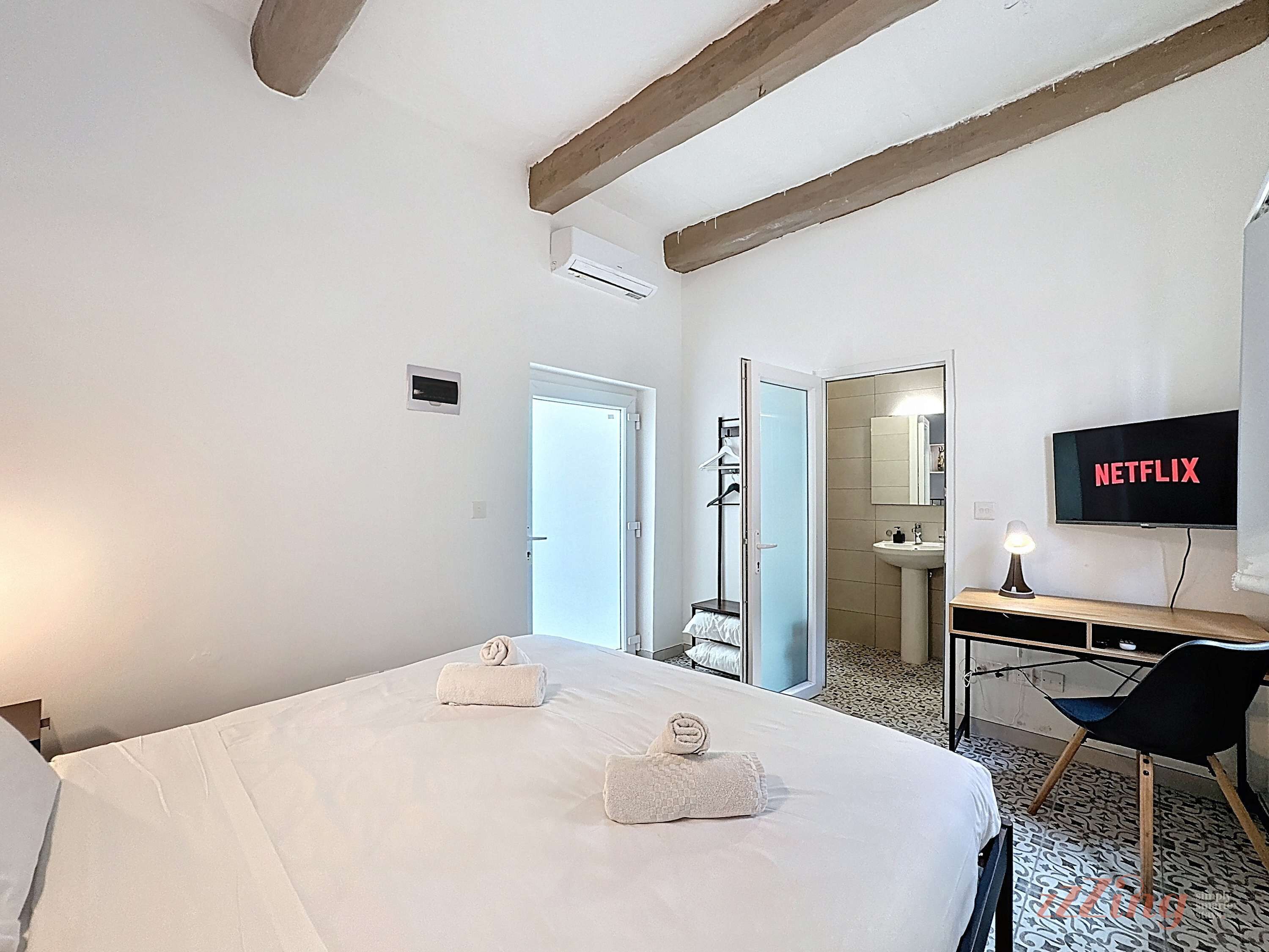 Hotelkamer met een bed, een bureau, een stoel, een televisietoestel waarop 'NETFLIX' wordt weergegeven, en een badkamer die door een open deur zichtbaar is.