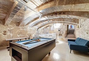 A pool table in a room with stone arches, a sofa, and a staircase leading to an upper level.