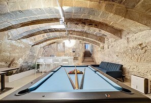 A pool table in a stone-walled room with a sofa and a bar area.