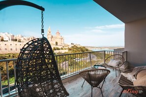 En balkon med fletmøbler, en hængekøjsstol og udsigt til en historisk bygning.