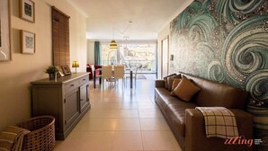 Un salon avec un canapé en cuir marron, un coin repas avec une table et des chaises, et une grande fresque abstraite sur le mur.
