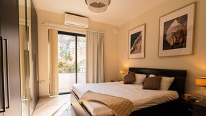 Une chambre d’hôtel avec un lit, deux tables de chevet, une fenêtre avec des rideaux et deux tableaux encadrés accrochés au mur.