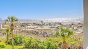 Blick auf einen Strand mit Palmen und Sträuchern im Vordergrund, ein Sandstrand und das Meer im Hintergrund.