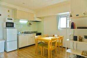 A compact kitchen with a dining area, white appliances, and a window with curtains.