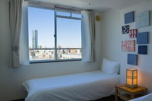 A hotel room with a bed, a nightstand, a window with curtains, and a city view.
