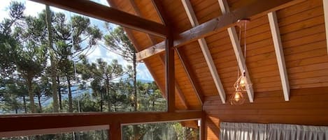 A wooden deck with a glass balustrade, a red cushioned sofa, and a hot tub.