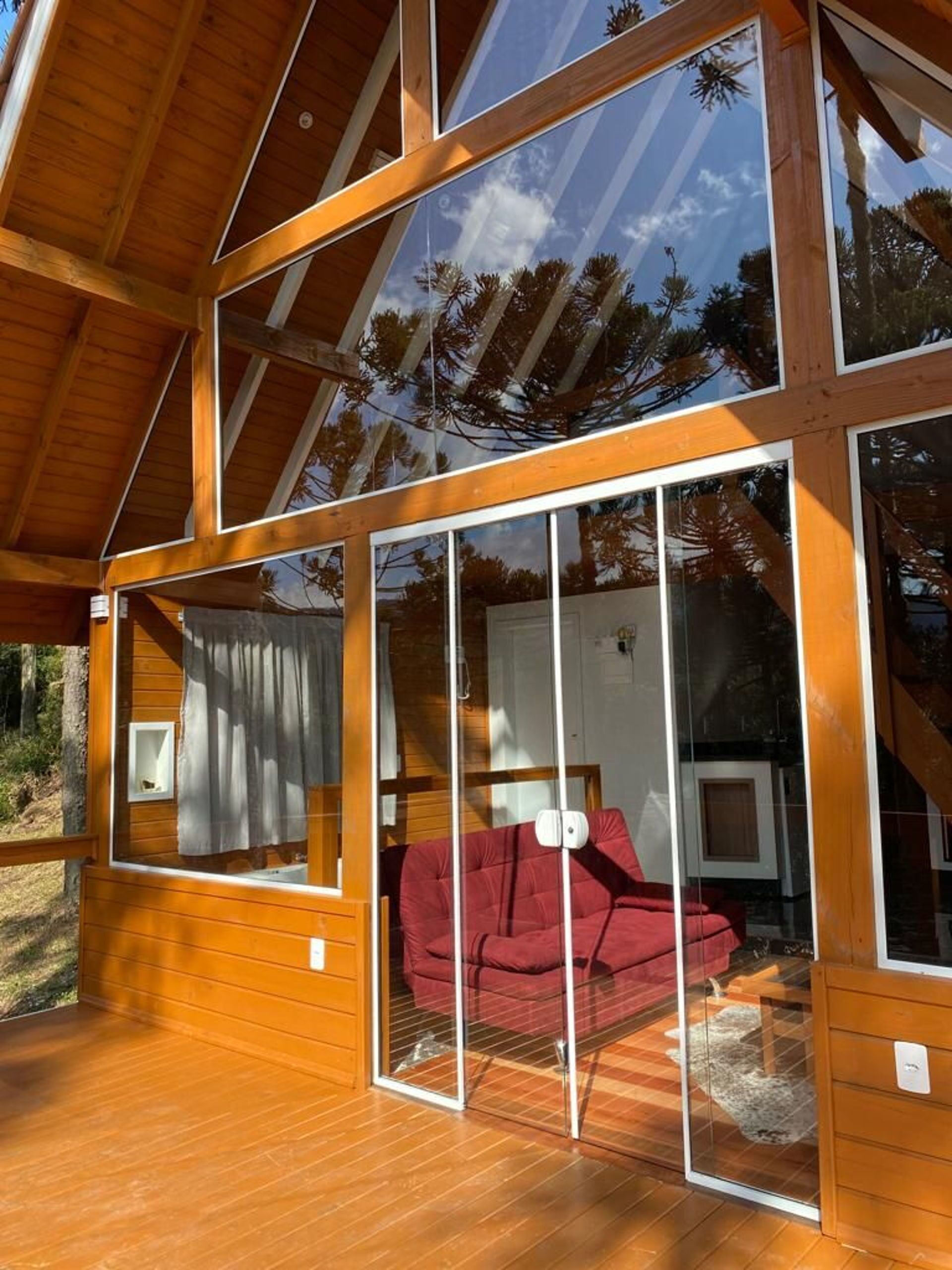 Une cabane en bois dotée de grandes portes vitrées qui donnent sur un espace de vie avec un canapé rouge et une cheminée.