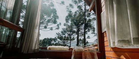 A hot tub with a glass of pink drink, wooden cabin interior, and a view of trees through the windows.