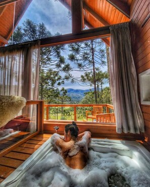 A person relaxing in a hot tub with a scenic view of trees and mountains.