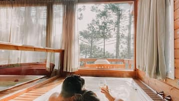 A wooden cabin with a large window, a hot tub, and a view of trees.