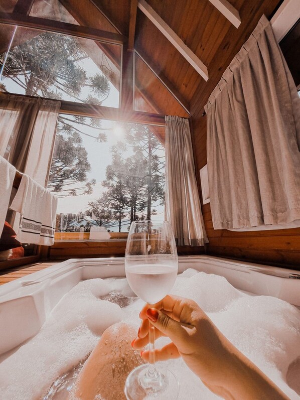 A room with a wooden ceiling, a large window with curtains, and a bathtub filled with bubbles.