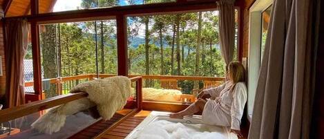 A cabin with a large window, a hot tub, and a wooden deck.