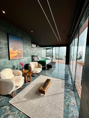 A modern living room with a large window, a painting, and a bed with a view.