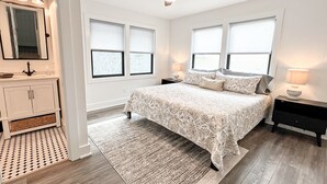 A bedroom with a bed, bedside tables, a ceiling fan, and a window with blinds. - Experience Ocean and Pier Views, Close proximity to the Sand, at this Luxury Bea (Wrightsville Beach)