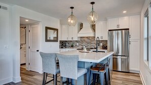 A modern kitchen with a central island, stainless steel appliances, and hanging pendant lights. - Experience Ocean and Pier Views, Close proximity to the Sand, at this Luxury Bea (Wrightsville Beach)