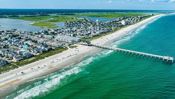 An aerial view of a coastal town with a long pier extending into the ocean, a sandy beach, and residential buildings along the shore. - Experience Ocean and Pier Views, Close proximity to the Sand, at this Luxury Bea (Wrightsville Beach)