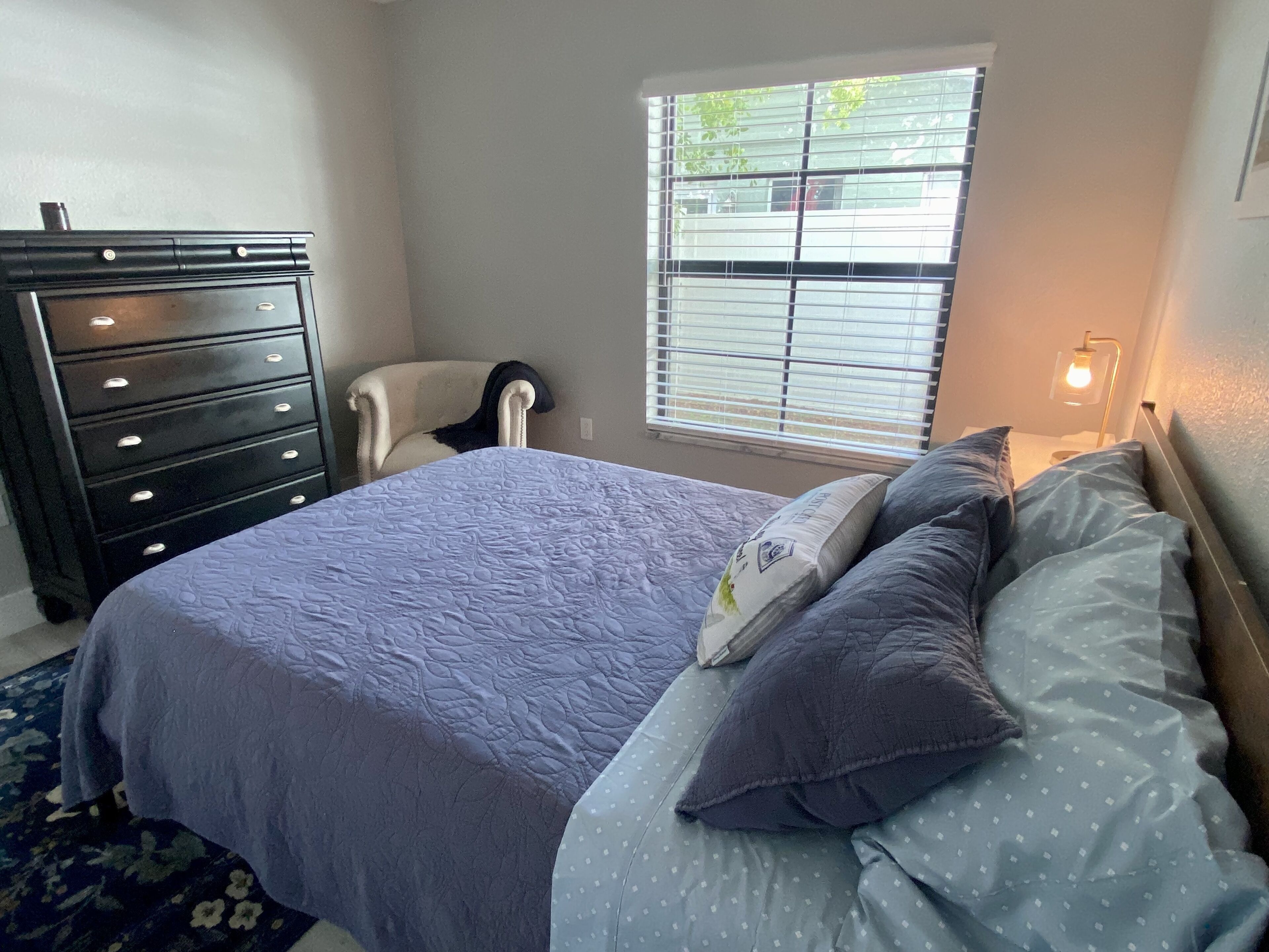 Une chambre à coucher comprenant un lit, une commode, une chaise, une fenêtre et une table de chevet.