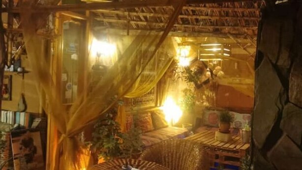 Une pièce chaleureuse avec un toit de chaume, un lit recouvert d’une courtepointe à motifs, une table de chevet avec une lampe et une fenêtre avec des rideaux.