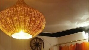 Un salon chaleureux avec une cheminée, un luminaire en fibres tressées, une maquette de bateau et un tapis coloré.