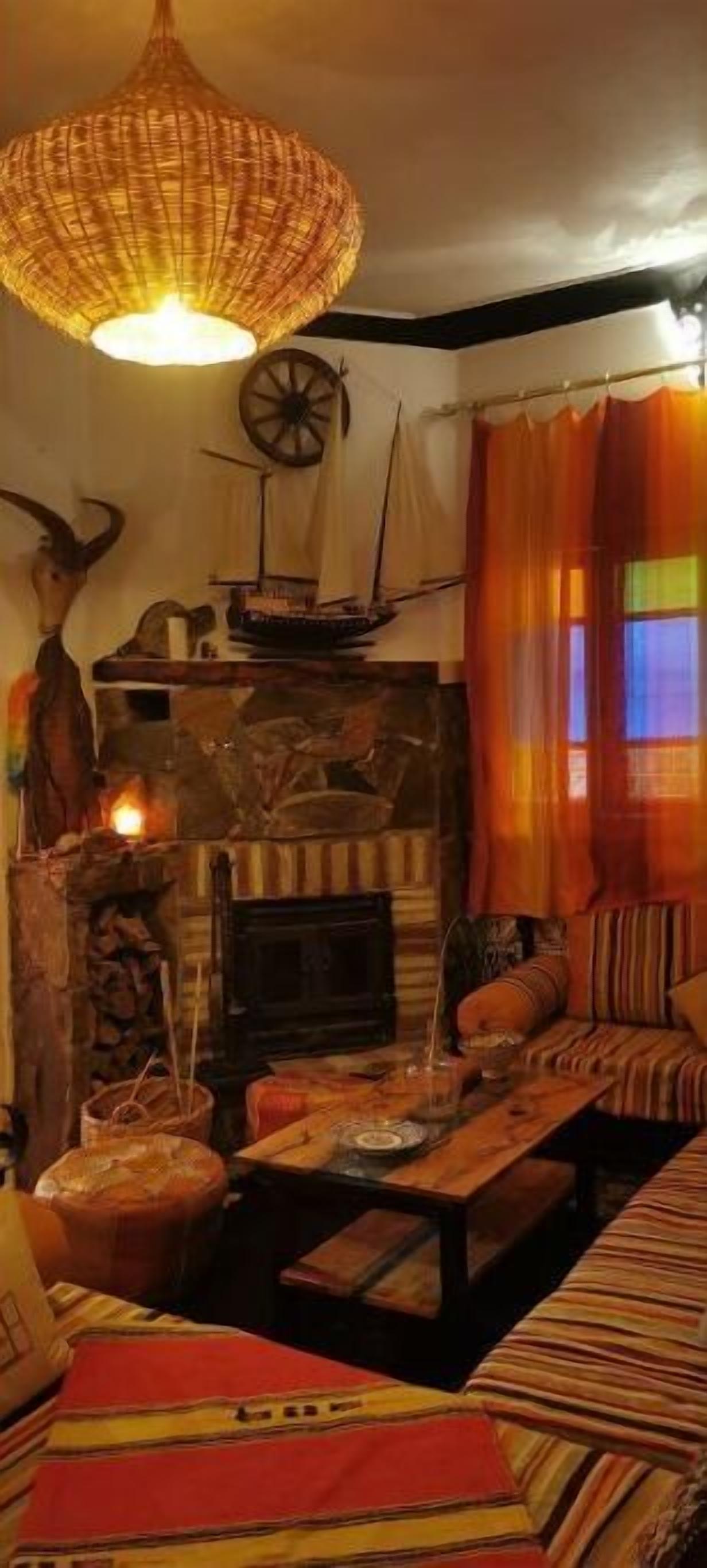 A cozy living room with a fireplace, a woven light fixture, a ship model, and a colorful rug.
