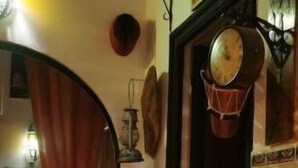 A cozy room with a patterned wall, a cushioned seating area, a wall-mounted clock, and a decorative lamp. - Atlas room (w) (Agadir)