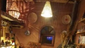 A cozy, dimly lit room with a wooden ceiling, a patterned sofa, a small table with a lamp, and various decorative items. - Atlas room (w) (Agadir)