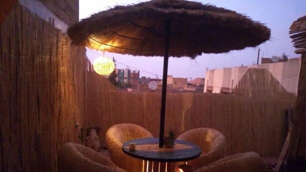 A cozy outdoor seating area with a round table and chairs, a thatched umbrella, and a warm light source. - Atlas room (w) (Agadir)