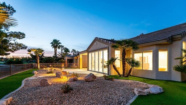 Una casa moderna con jardín ajardinado, que cuenta con un patio con rocas y palmeras.