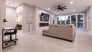 Una sala de estar moderna con un sofá, un televisor montado en la pared y un ventilador de techo.