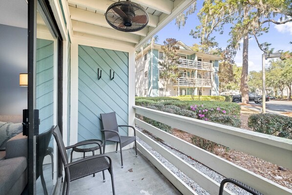 A balcony with wicker chairs, a ceiling fan, and a view of a building with balconies and a landscaped garden. - Fully Renovated, First Floor Villa "Just Beachy" (Hilton Head Island)