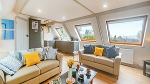 A spacious living room with a high ceiling, two sofas with cushions, a coffee table with books and a vase, and large windows offering views of the outdoors. - 1 bedroom accommodation in Burraton, near Ivybridge (Burraton, near Ivybridge)