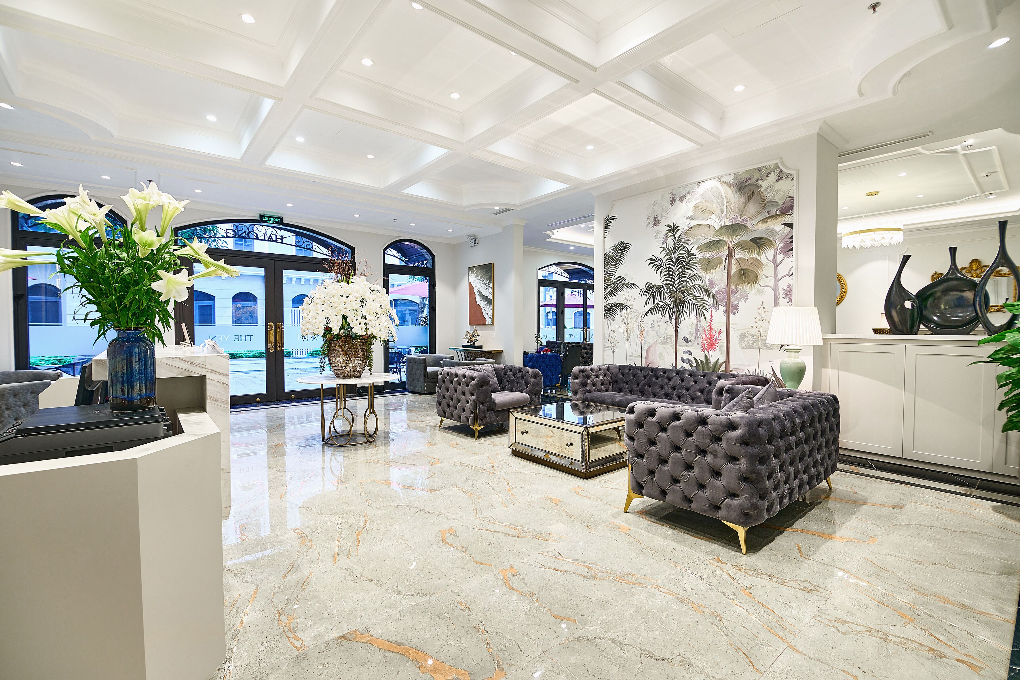 A spacious lobby with a marble floor, tufted sofas, a reception desk, and a large window with a view of the outside.