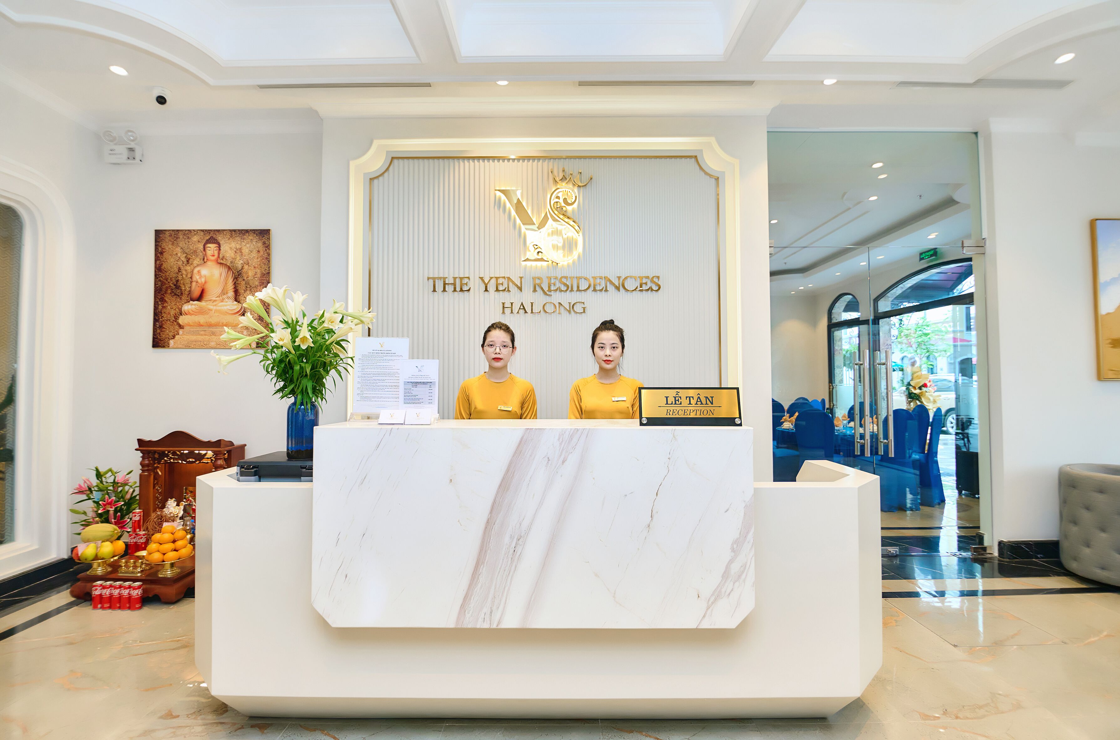 A reception desk at The Yen Residences Halong with a Buddha painting, a floral arrangement, and a sign indicating the reception area.