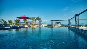Ein Pool mit unendlicher Optik auf dem Dach, mit Palmen, Liegestühlen und einem roten Sonnenschirm.
