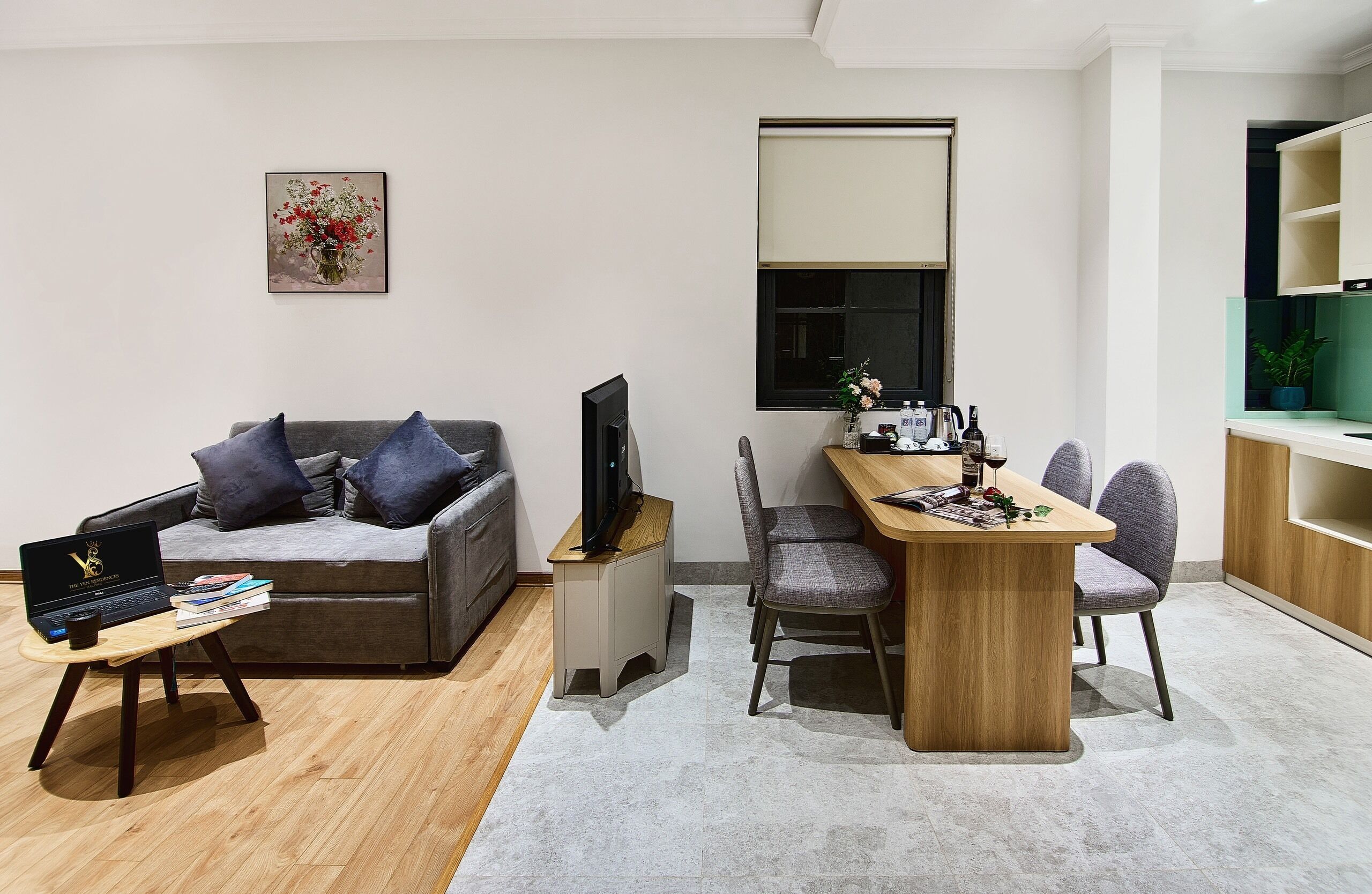 A modern living room with a grey sofa, a wooden coffee table, a TV, and a dining area with a wooden table and chairs.