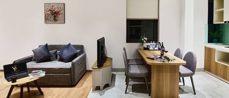 A modern living room with a grey sofa, a wooden coffee table, a TV, and a dining area with a wooden table and chairs.
